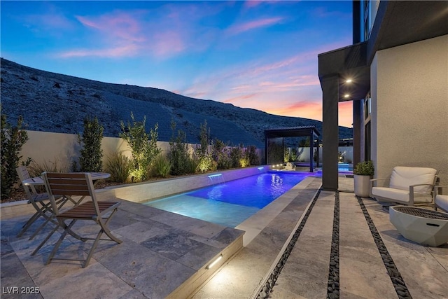 pool at dusk featuring a patio, a mountain view, and pool water feature