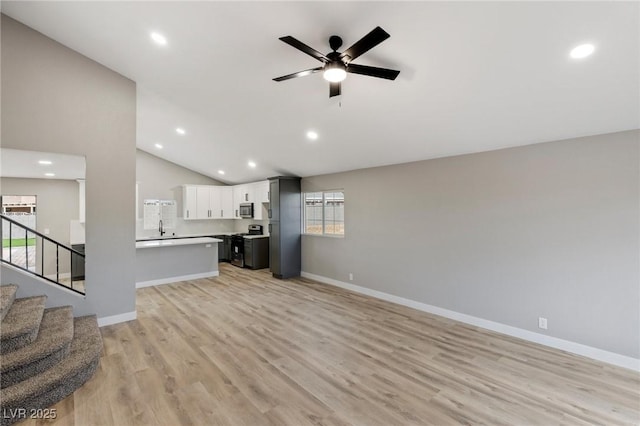 unfurnished living room featuring ceiling fan, sink, vaulted ceiling, and light hardwood / wood-style flooring