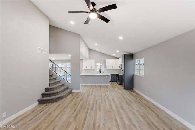 unfurnished living room with ceiling fan, high vaulted ceiling, sink, and light wood-type flooring