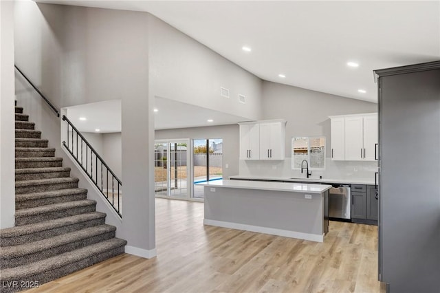 kitchen with a kitchen island, white cabinets, decorative backsplash, stainless steel dishwasher, and light hardwood / wood-style flooring