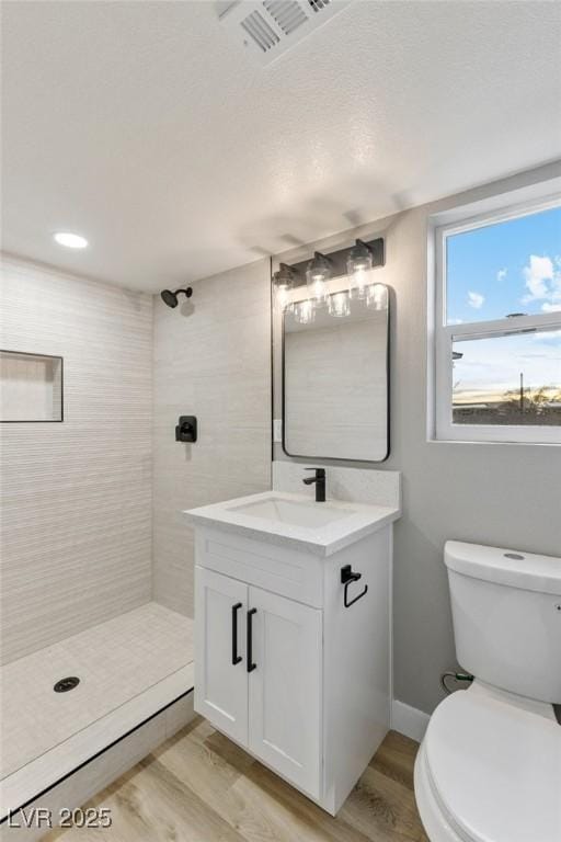 bathroom with hardwood / wood-style flooring, tiled shower, vanity, and toilet