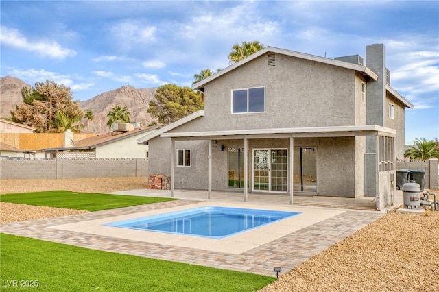 back of property with a fenced in pool, a mountain view, a patio, and a lawn