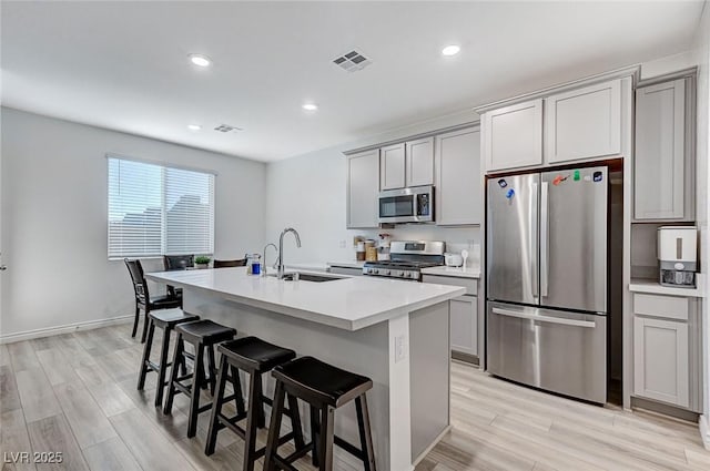 kitchen with an island with sink, stainless steel appliances, sink, and gray cabinetry