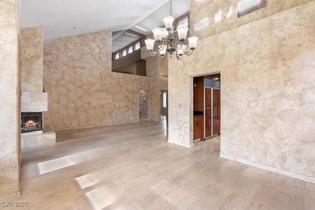 unfurnished dining area featuring high vaulted ceiling, a high end fireplace, and a notable chandelier