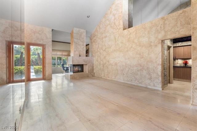 unfurnished living room featuring a multi sided fireplace and a towering ceiling