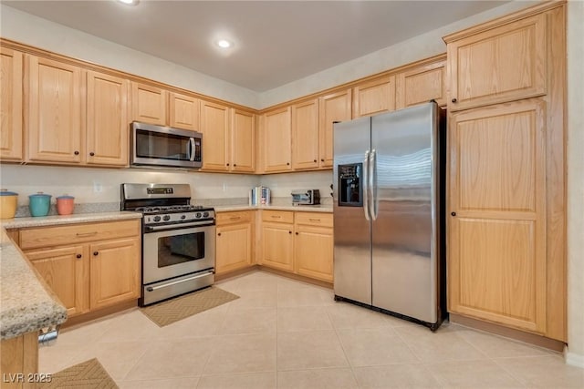 kitchen featuring stainless steel appliances, light tile patterned floors, light stone counters, and light brown cabinetry