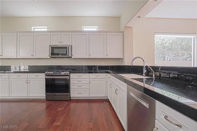 kitchen with sink, white cabinetry, dark stone countertops, dark hardwood / wood-style flooring, and stainless steel appliances