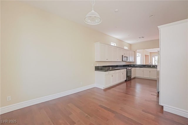 kitchen with appliances with stainless steel finishes, sink, white cabinets, hanging light fixtures, and dark wood-type flooring