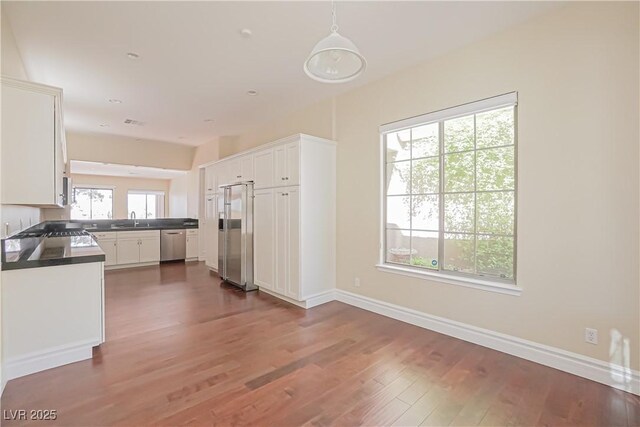 kitchen with wood finished floors, dark countertops, white cabinets, a sink, and appliances with stainless steel finishes