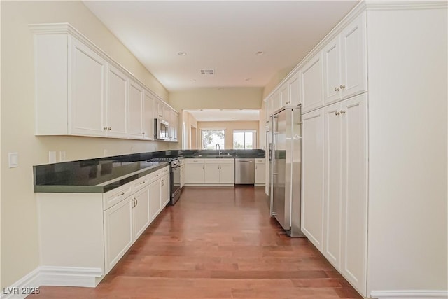 kitchen featuring wood finished floors, dark countertops, white cabinets, a sink, and stainless steel appliances