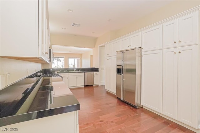 kitchen with stainless steel appliances, sink, hardwood / wood-style floors, and white cabinets