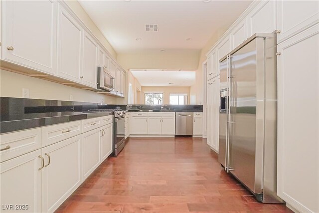 kitchen with dark countertops, white cabinets, stainless steel appliances, and wood finished floors