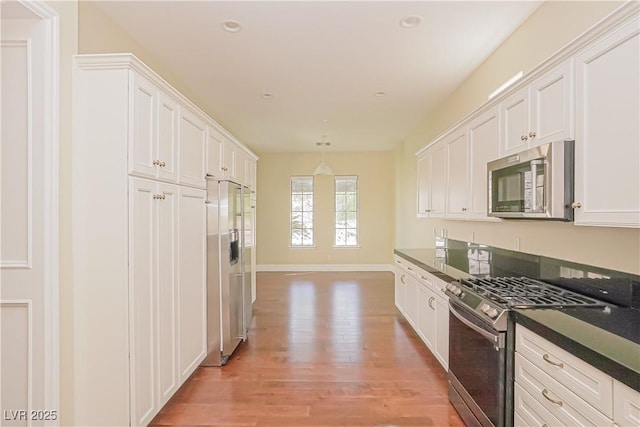 kitchen with dark countertops, light wood finished floors, stainless steel appliances, decorative light fixtures, and white cabinetry