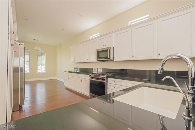 kitchen with sink, white cabinetry, hanging light fixtures, appliances with stainless steel finishes, and dark hardwood / wood-style floors