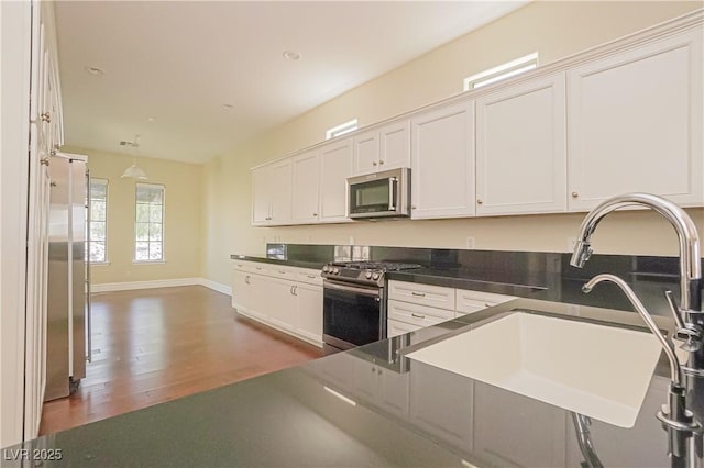 kitchen with white cabinets, stainless steel appliances, dark countertops, and a sink