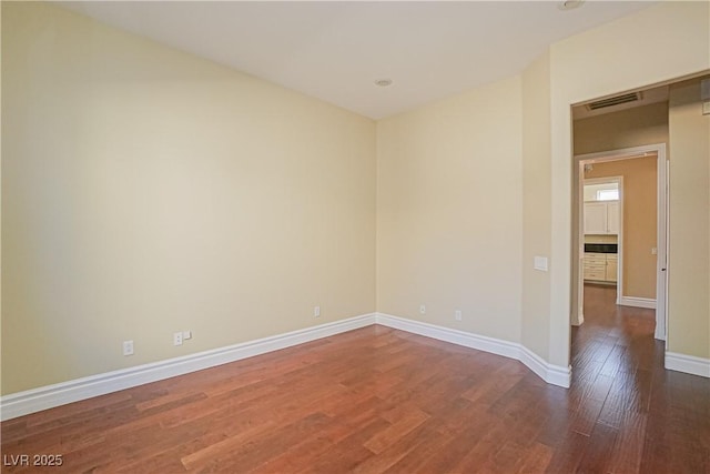 spare room with baseboards, dark wood-style flooring, and visible vents