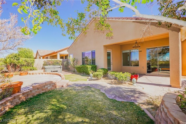 rear view of property featuring a hot tub, a patio area, and a lawn