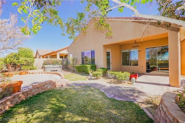 rear view of property with fence, a hot tub, stucco siding, a lawn, and a patio