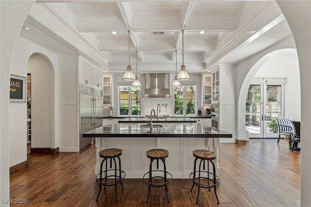 kitchen with pendant lighting, built in refrigerator, white cabinetry, range hood, and a kitchen breakfast bar