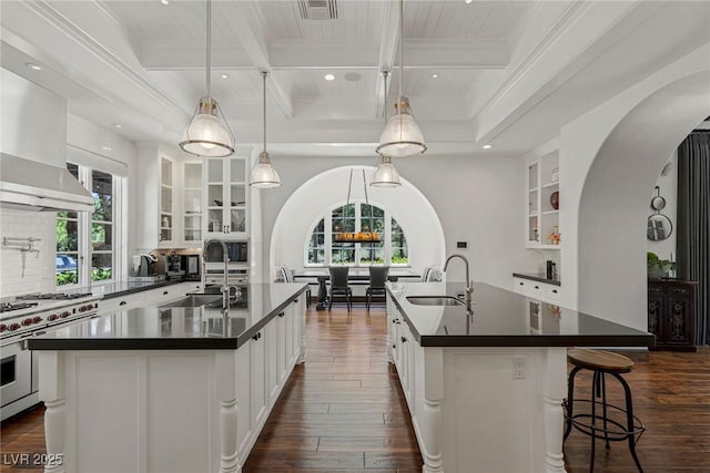 kitchen with sink, tasteful backsplash, double oven range, an island with sink, and pendant lighting