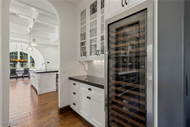 wine room featuring dark hardwood / wood-style flooring, coffered ceiling, beverage cooler, and beam ceiling