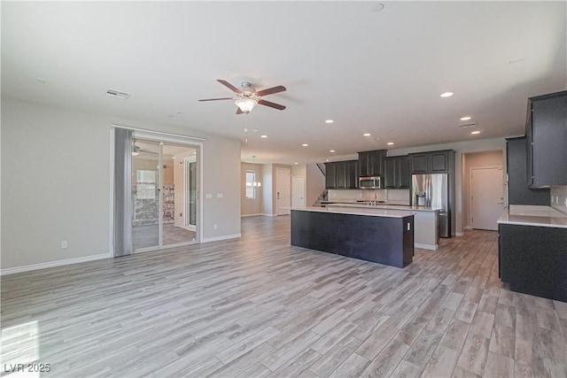 kitchen with light hardwood / wood-style flooring, a center island with sink, ceiling fan, and appliances with stainless steel finishes