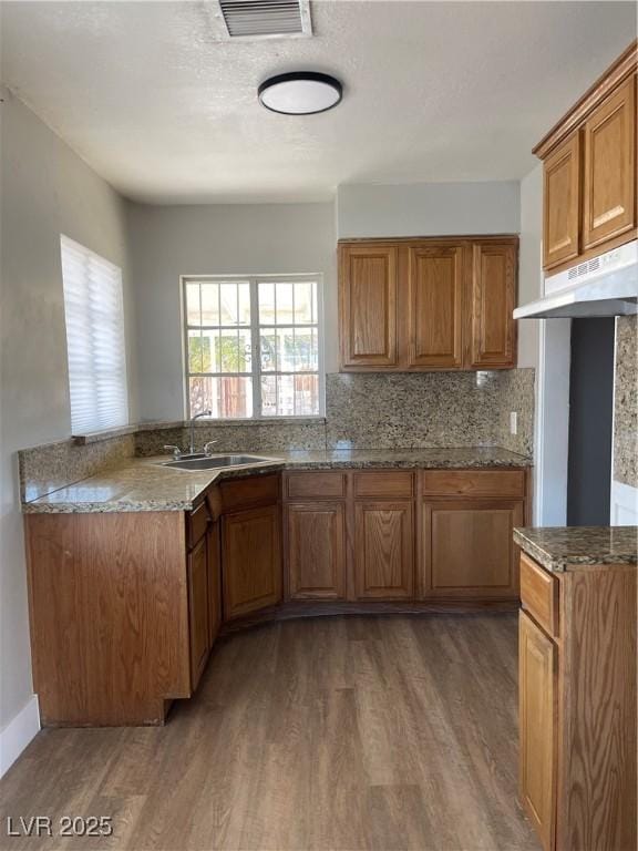 kitchen with stone counters, sink, backsplash, dark hardwood / wood-style flooring, and kitchen peninsula