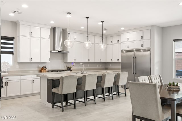 kitchen featuring appliances with stainless steel finishes, pendant lighting, a breakfast bar area, a kitchen island with sink, and wall chimney range hood