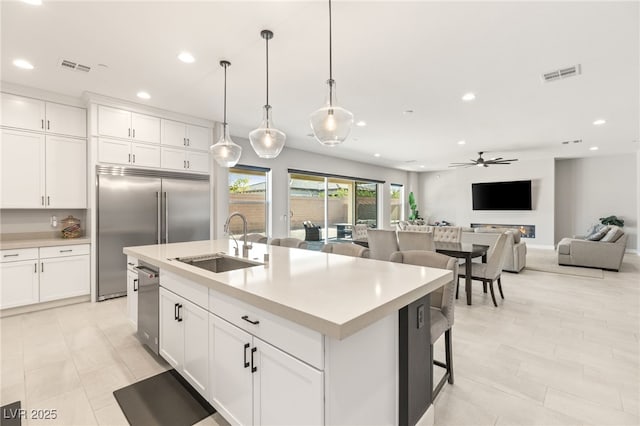 kitchen with decorative light fixtures, white cabinetry, an island with sink, sink, and stainless steel appliances