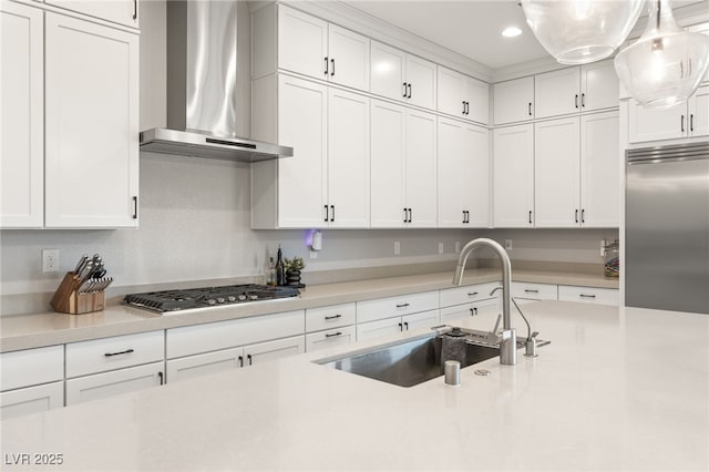 kitchen featuring appliances with stainless steel finishes, decorative light fixtures, sink, white cabinets, and wall chimney range hood