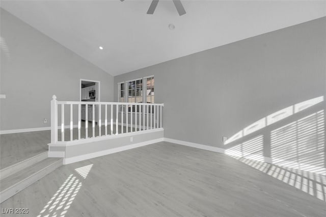 spare room featuring high vaulted ceiling, wood finished floors, a ceiling fan, and baseboards