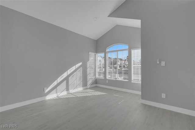 spare room featuring high vaulted ceiling, baseboards, and wood finished floors