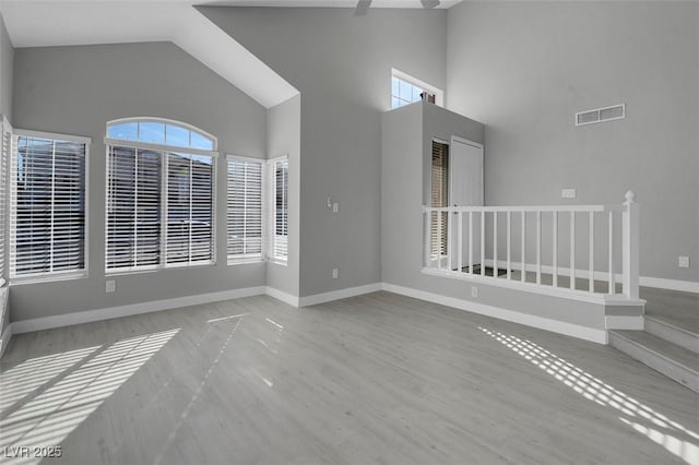 unfurnished room with high vaulted ceiling, wood finished floors, a ceiling fan, visible vents, and baseboards