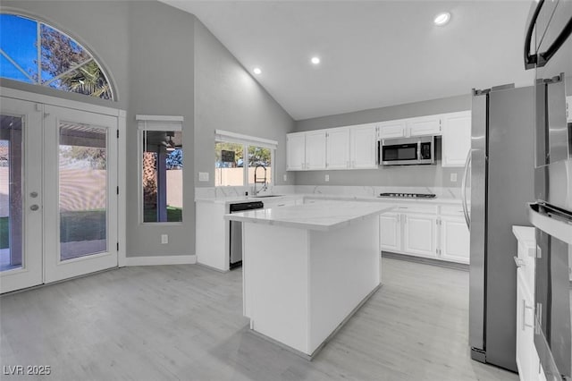 kitchen with stainless steel appliances, light wood finished floors, a kitchen island, and white cabinetry