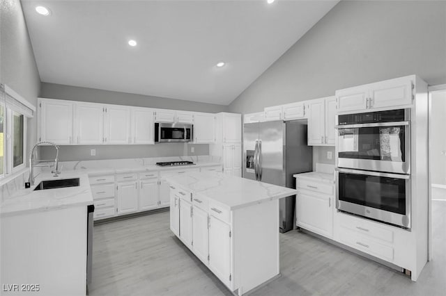 kitchen featuring appliances with stainless steel finishes, light stone counters, a center island, white cabinetry, and a sink