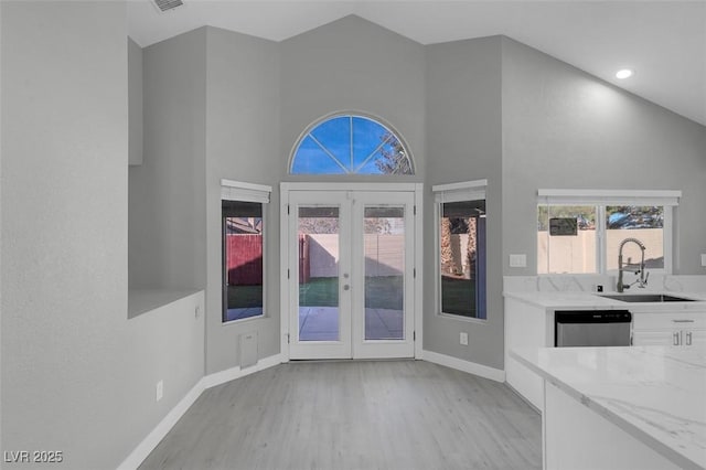 unfurnished dining area with french doors, light wood-style floors, a sink, high vaulted ceiling, and baseboards