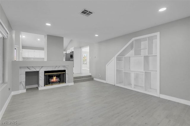 unfurnished living room with a premium fireplace, light wood-type flooring, visible vents, and recessed lighting