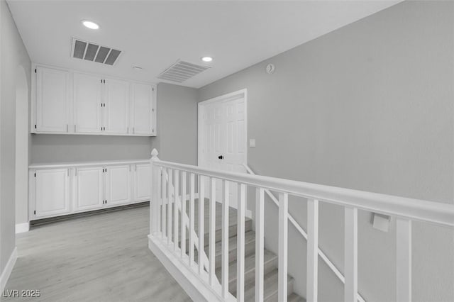 corridor with light wood-style floors, wainscoting, visible vents, and an upstairs landing