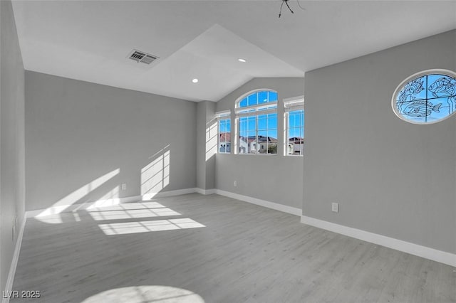 empty room with lofted ceiling, baseboards, visible vents, and wood finished floors