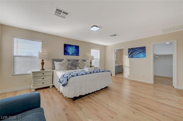 bedroom with ensuite bath, a spacious closet, a closet, and light hardwood / wood-style flooring