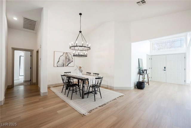 dining space featuring a towering ceiling, a chandelier, and light hardwood / wood-style floors