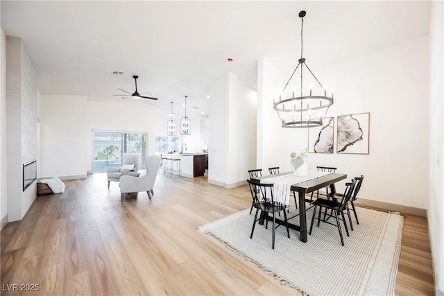 dining area with sink, ceiling fan with notable chandelier, and light hardwood / wood-style flooring