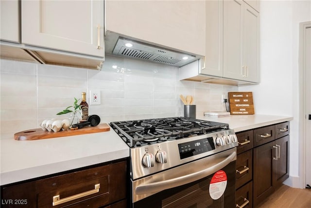 kitchen featuring dark brown cabinetry, stainless steel gas range, white cabinetry, tasteful backsplash, and wall chimney range hood