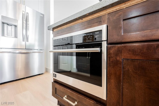 kitchen featuring appliances with stainless steel finishes, dark brown cabinets, and light wood-type flooring