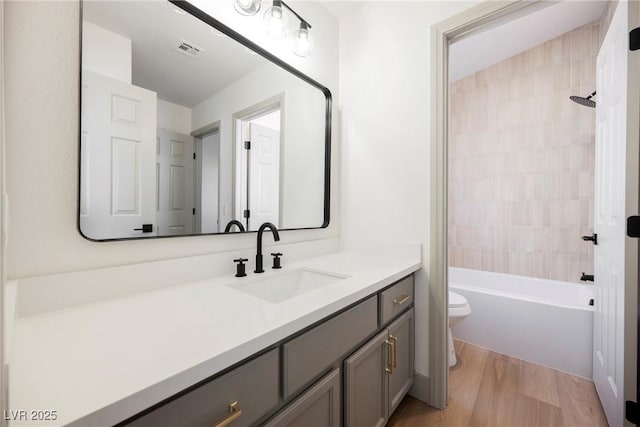 full bathroom featuring vanity, hardwood / wood-style floors, tiled shower / bath combo, and toilet