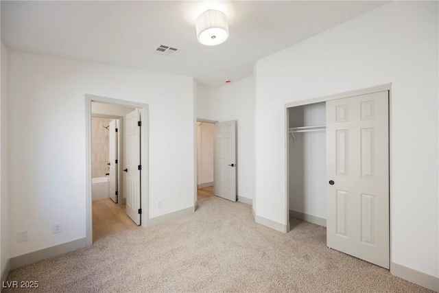 unfurnished bedroom with light colored carpet, ensuite bathroom, and a closet