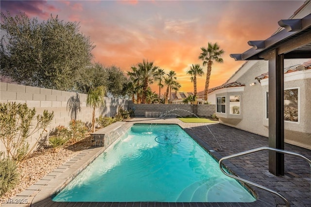 pool at dusk with pool water feature and a patio area