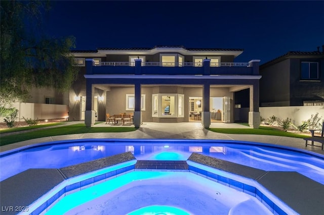 pool at night with an in ground hot tub and a patio