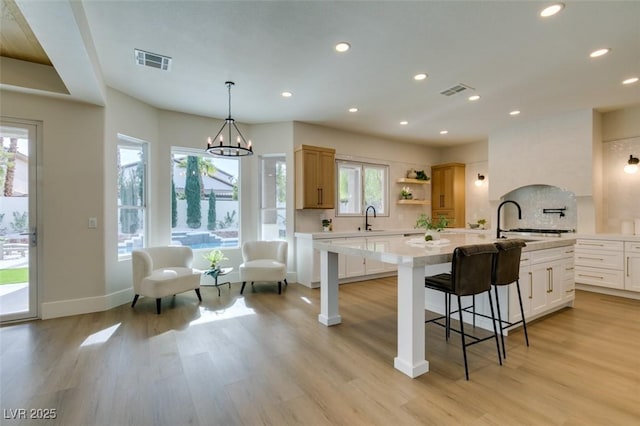 kitchen with sink, a center island with sink, white cabinets, and light wood-type flooring