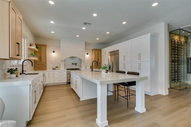 kitchen with backsplash, a breakfast bar area, light hardwood / wood-style floors, and an island with sink